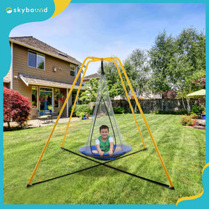 A boy is sitting on the swing of the yellow swing set in the yard.