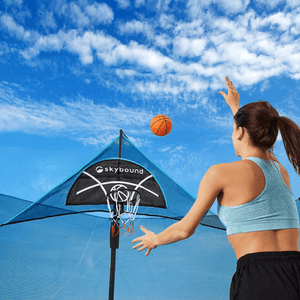 A woman is shooting basketball in to a trampoline basketball hoop from the SkyBound brand.